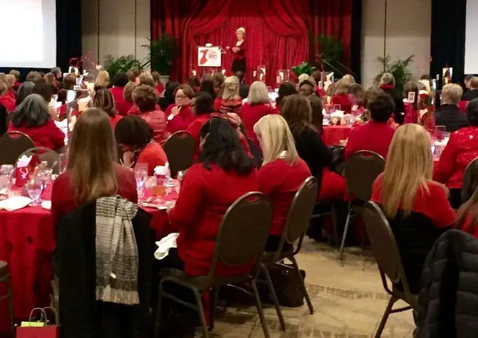 A full ballroom of women in red at a Go Red for Women luncheon where Diana is speaking
