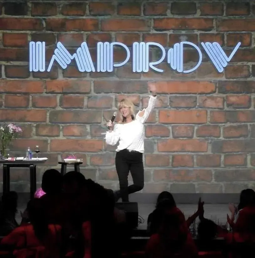 Diana Jordan performing stand-up under the neon Improv sign
